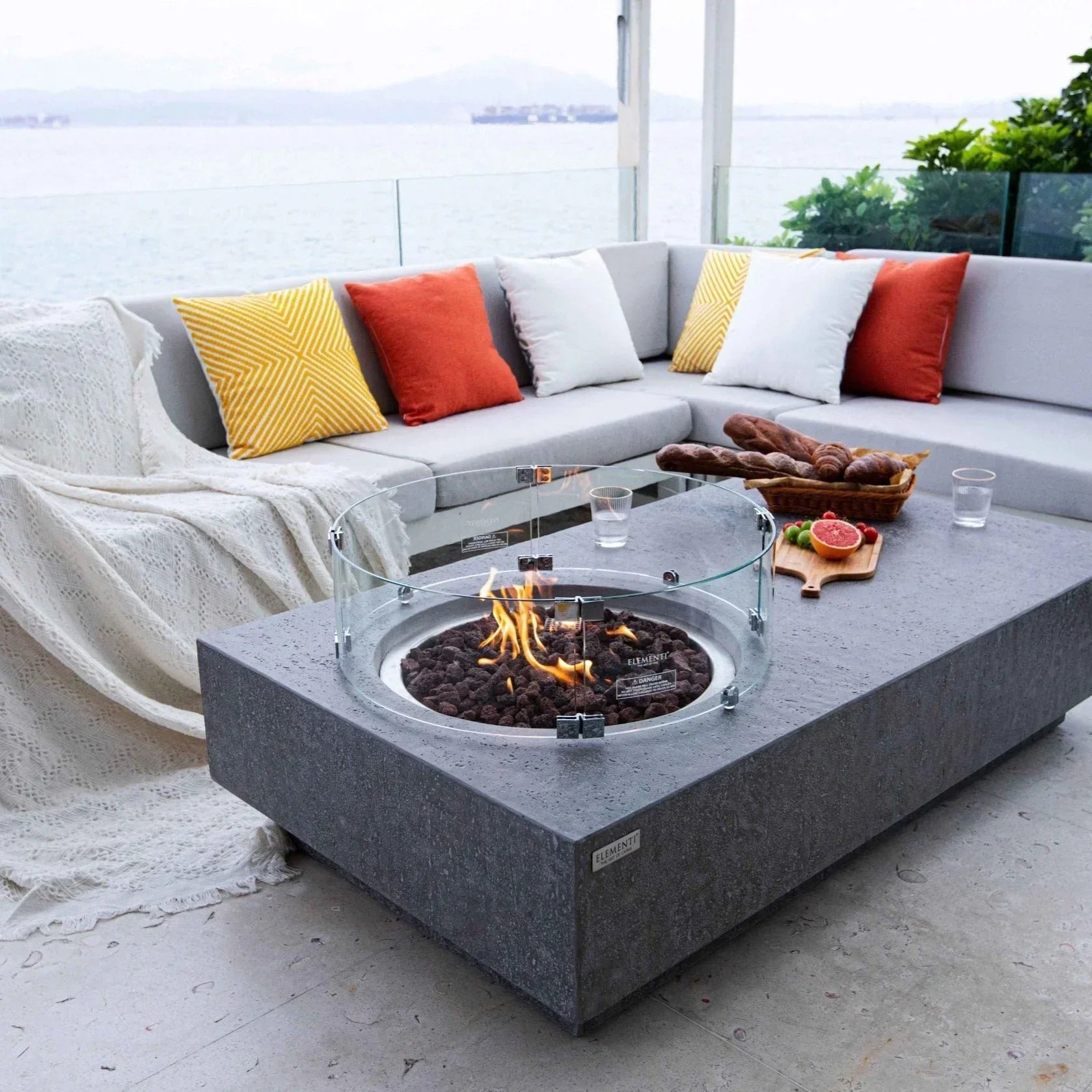 Elementi Metropolis fire pit table light gray on patio with sectional sofa and colorful pillows
