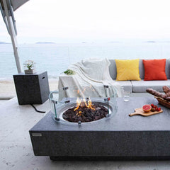 Elementi Metropolis fire pit table with glass windscreen on a patio by the ocean, modern outdoor seating