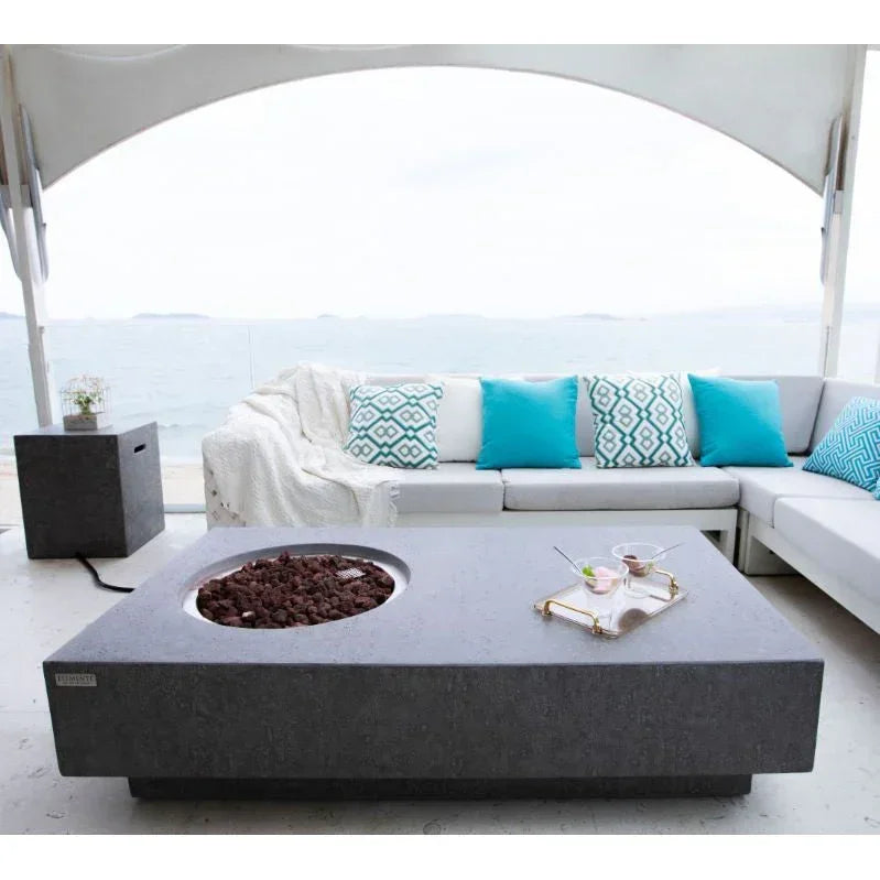 Metropolis rectangular outdoor fire pit table on patio with ocean view, modern sofa and blue pillows