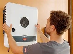 Fronius wall-mounted solar inverter being installed by a man, energy equipment