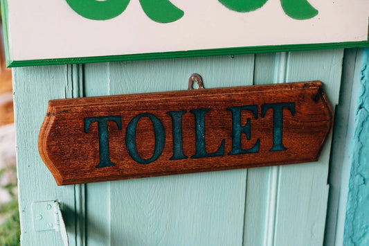 Wooden toilet sign with blue lettering on a light green wall, eco-friendly setting